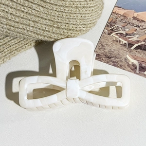 Close-up of elegant cream white marble pattern bow hair claw clip on beige knit background