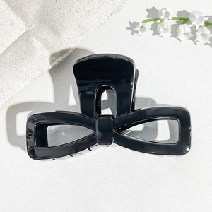 Detail view of a black glossy UV finish bow hair claw clip on a white leather background