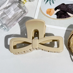 Macro detail of cream bow-shaped hair claw clip with smooth finish on a minimalist desk