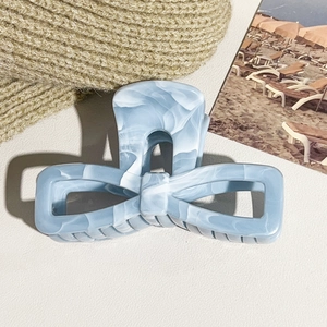 Detailed view of blue marble bow hair claw clip on soft beige textured background