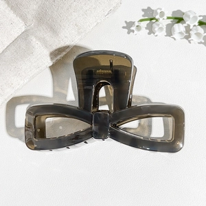 Close-up of translucent dark grey bow hair claw clip with lily of the valley background