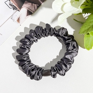 Detail of silk-like black scrunchie with a sleek buckle on white leather background