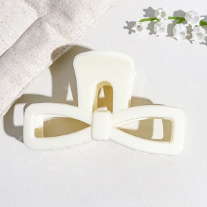 Close-up of cream white bow hair claw clip with glossy UV finish on leather background