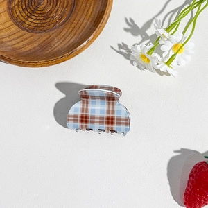 Close-up of blue and brown checkered hair claw clip on a white leather background