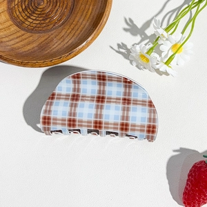 Detail view of a brown and blue plaid hair claw clip on a textured white background