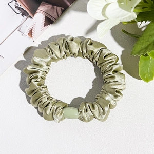 Detailed view of light green silk satin scrunchie with decorative bead on white background