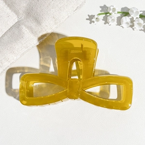 Detail shot of a translucent ginger yellow bow-shaped hair claw clip on a textured surface