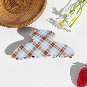 Detailed view of a plaid hair claw clip in blue and brown on a minimalist background