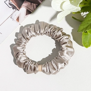 Detailed close-up of champagne silk scrunchie with pleated texture on white leather