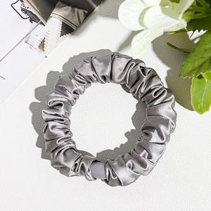 Close-up of a silver-grey satin silk scrunchie with elegant pleated texture on leather