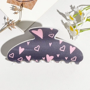 Detailed view of grey hair claw clip with pink heart patterns on white leather background