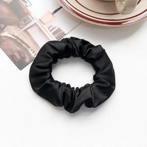 Close-up of black silk scrunchie with satin texture on white minimalist background