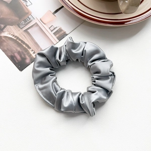 Detail showing the silky texture and fine stitching of a silver-grey satin scrunchie