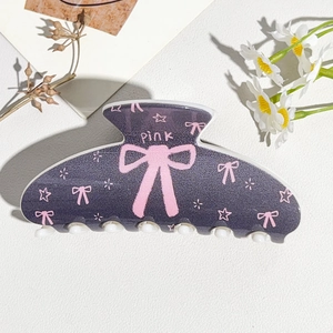 Close-up of semi-round hair claw clip with pink bow and star patterns on purple matte surface