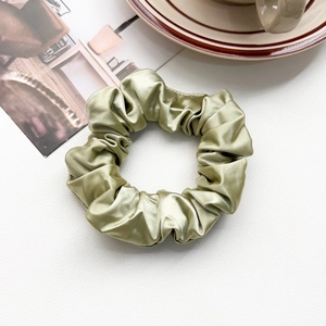Detailed view of pale green silk scrunchie with soft satin luster on a white textured surface