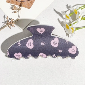 Detail of purple glitter hair claw with pink heart patterns and 'Nice day' typography