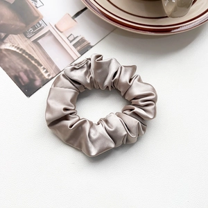 Close-up of champagne silk scrunchie with soft folds on a textured leather background
