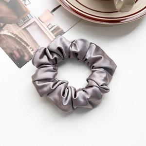 Flat lay of a silver grey silk scrunchie on white leather with coffee cup decor