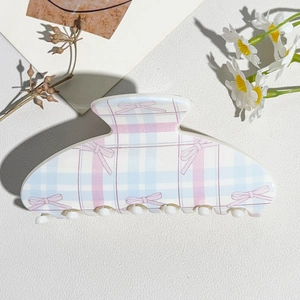 Detail view of large blue plaid hair claw clip with pink bow patterns on white background
