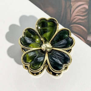 Macro shot of green heart-shaped resin petals with gold edges on a floral hair claw clip