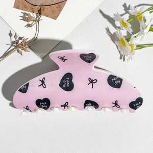 Detail shot of pink square claw clip featuring black heart prints and Nice day text