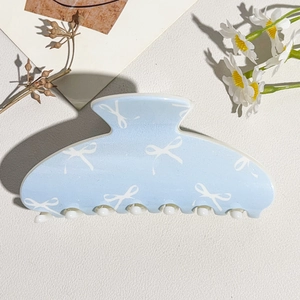 Detail of light blue hair claw clip with white bow patterns and resin finish
