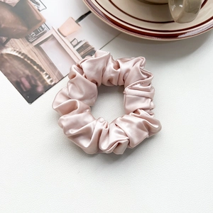 Close-up of light pink seamless silk scrunchie on elegant white leather background