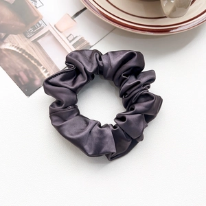 Macro shot of dark purple silk scrunchie showing glossy satin texture and pleats