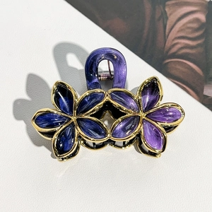 Detailed top view of purple floral hair claw clip with golden edges on white texture