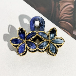 Detailed macro view of dual blue floral hair claw clips with gold metal frames and resin petals