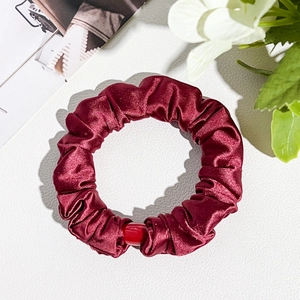 Detail of burgundy satin hair scrunchie with smooth pleated texture and accent bead