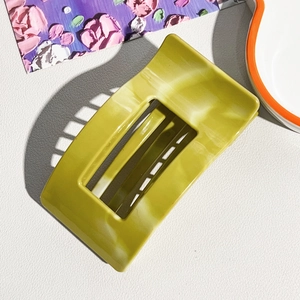 Detail of large olive green marble patterned silicone hair claw clip on textured background