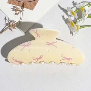 Detail of a large cream hair claw clip with pink bows and white rounded teeth