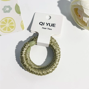 Détail du chouchou en satin vert avec texture soyeuse et perle sur emballage blanc