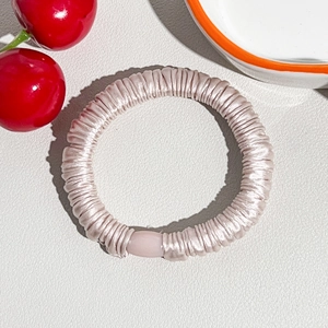 Detail of a champagne pink silk scrunchie with pleated texture and oval bead ornament