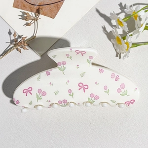 Detail of cream hair claw clip with pink tulip and bow pattern on textured surface