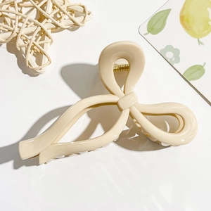 Macro detail of a cream bow hair claw clip with glossy finish and gold metal spring