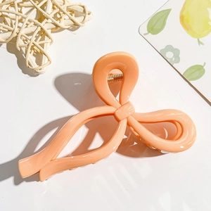 Detail view of the peach bow hair claw clip showing glossy resin and gold metal spring