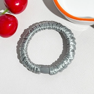 Detail of silver silk scrunchie with smooth texture and high elasticity on a white surface
