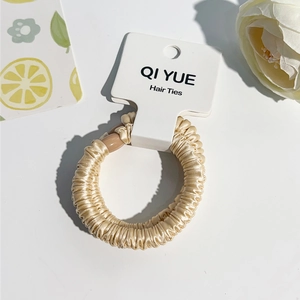 Gros plan du chouchou en satin doré champagne avec texture plissée et emballage