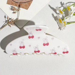 Detail of cream hair claw clip with pink cherry and heart patterns on textured background