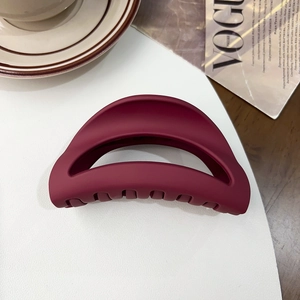 Macro shot of matte dark burgundy semicircular hair claw clip on elegant leather surface