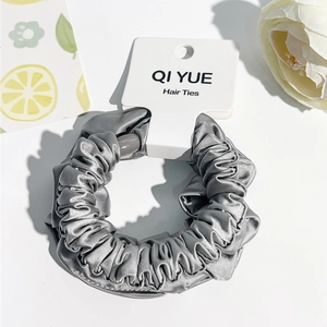 Détail d'un chouchou en satin gris plissé avec texture soyeuse et étiquette de marque