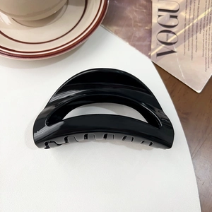 Detailed macro of black glossy hair claw clip next to a magazine on a white desk