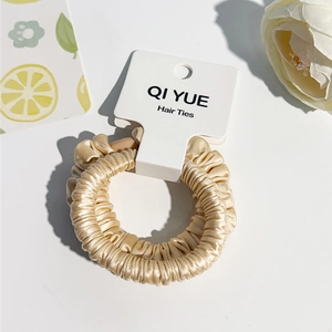 Détail du chouchou en satin champagne avec texture en soie plissée et bords ondulés