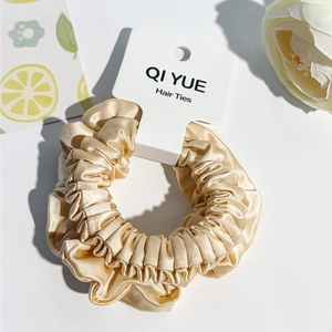 Gros plan sur chouchou en satin champagne avec texture froncée et étiquette de marque