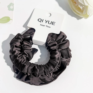 Détail d'un chouchou en satin noir plissé avec étiquette de marque et texture soyeuse