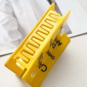 Detail shot of a yellow hair claw clip with Caution lettering and metal spring mechanism
