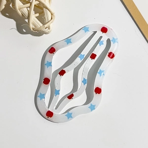 Dettaglio del fermaglio a onde color crema con motivi a mela rossa e stella blu