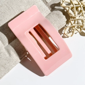 Detail view of 9.5cm rectangular pink hair claw clip with cutout stripes on linen background